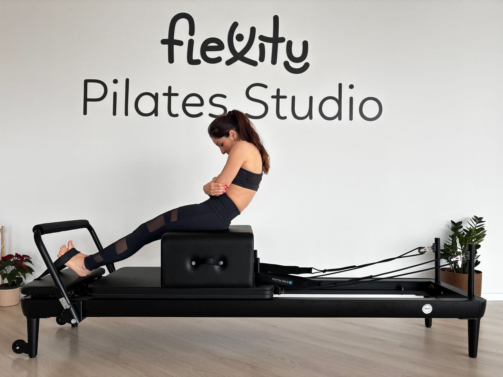woman practicing reformer pilates in a bright studio with wooden floors