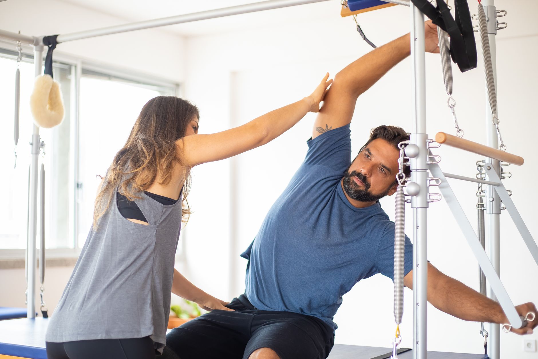 instructor correcting student posture on reformer pilates equipment